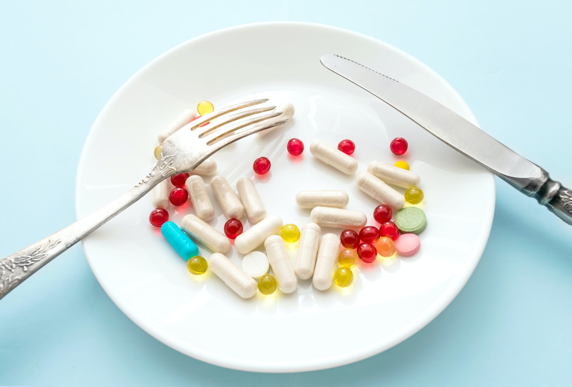 Many different weight loss pills and supplements as food on round white plate with fork and knife